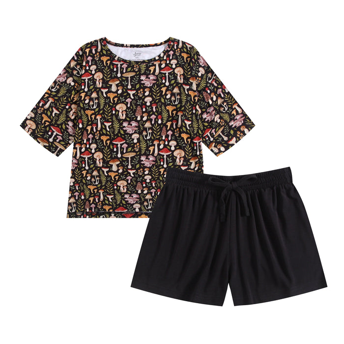 The Mystic Mushrooms Comfy Cloud Short Set by Jammie Session features a black short-sleeve top with a vibrant mushroom and leaf print, paired with plain black shorts.