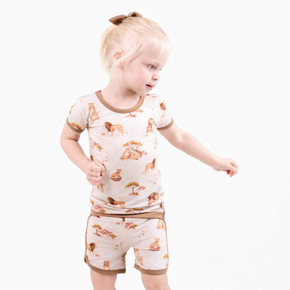 A young child with blonde hair in a ponytail wears the Ari (Lion) TENCEL‚Ñ¢ Modal Short Pajama Set by Jammie Session, crafted from buttery soft, hypoallergenic fabric, standing against a plain white background.