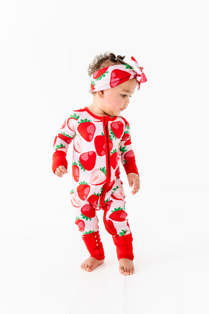 A toddler in a Jammie Session Berry Sweet (Strawberry) Romper with a matching headband stands against a plain white background.