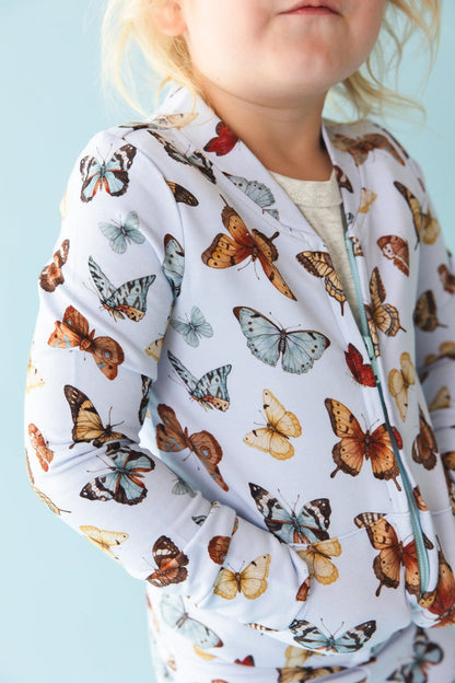 A child models the Jammie Session Butterfly Kisses Kids' Jacket‚Äîfeaturing colorful butterfly prints‚Äîagainst a light blue background.