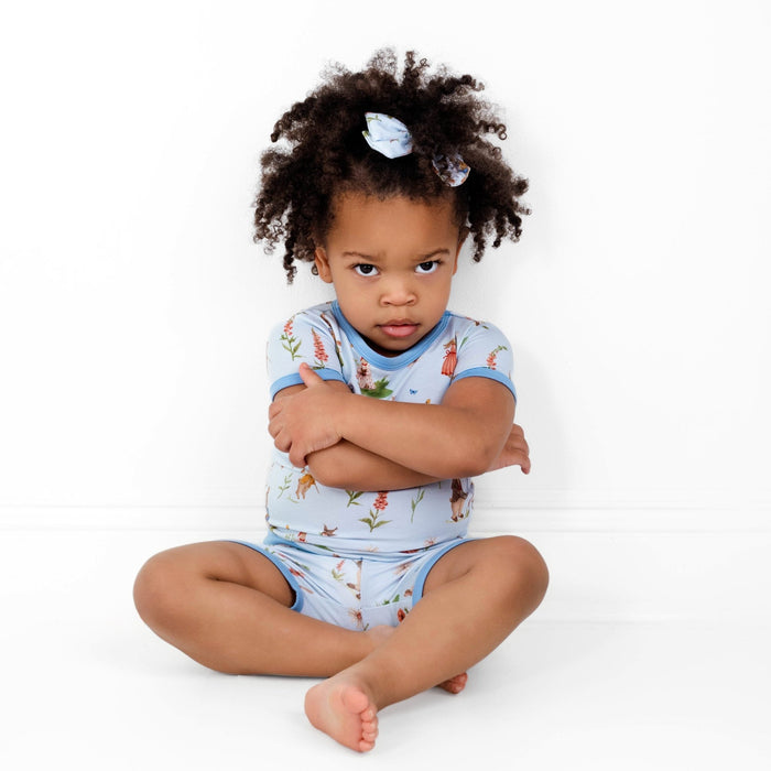 A young child with curly hair sits on the floor, arms crossed, wearing the Jammie Session "Don‚Äôt Worry, Be Hoppy (Rabbit)" Short Pajama Set and a matching bow, looking seriously at the camera.
