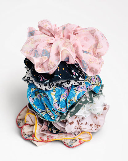 A stack of Jammie Session Handmade Scrunchies in colorful and floral designs, including silk options‚Äîperfect for work-at-home moms‚Äîarranged on a white background.