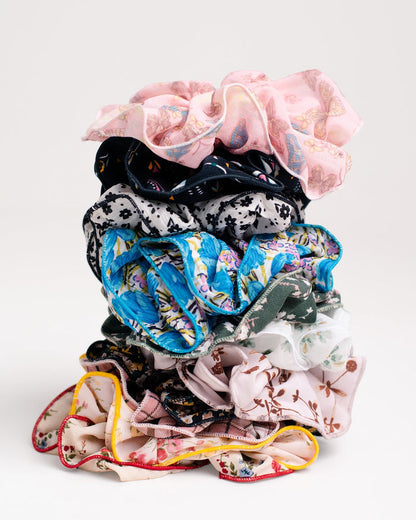 A stack of Jammie Session Handmade Scrunchies, including silk pieces with floral and patterned designs, crafted by work-at-home moms, displayed against a plain white background.