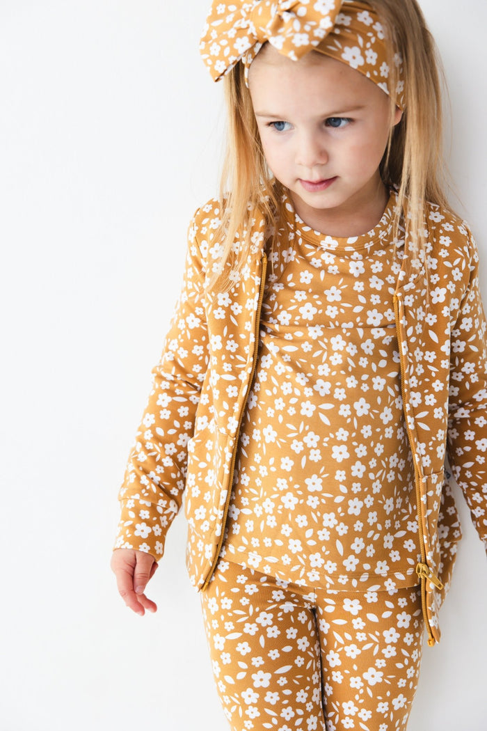 A young girl, styled in the Jammie Session Honey Blooms Kids' Jacket (runs small, please size up), wears a matching mustard-yellow floral outfit and headband, standing against a plain white background.