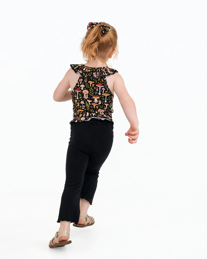 A young child with light hair walks away on a white background, wearing the Jammie Session Mystic Mushrooms Bloomy Crop Set‚Äî a black printed sleeveless top and matching pants.