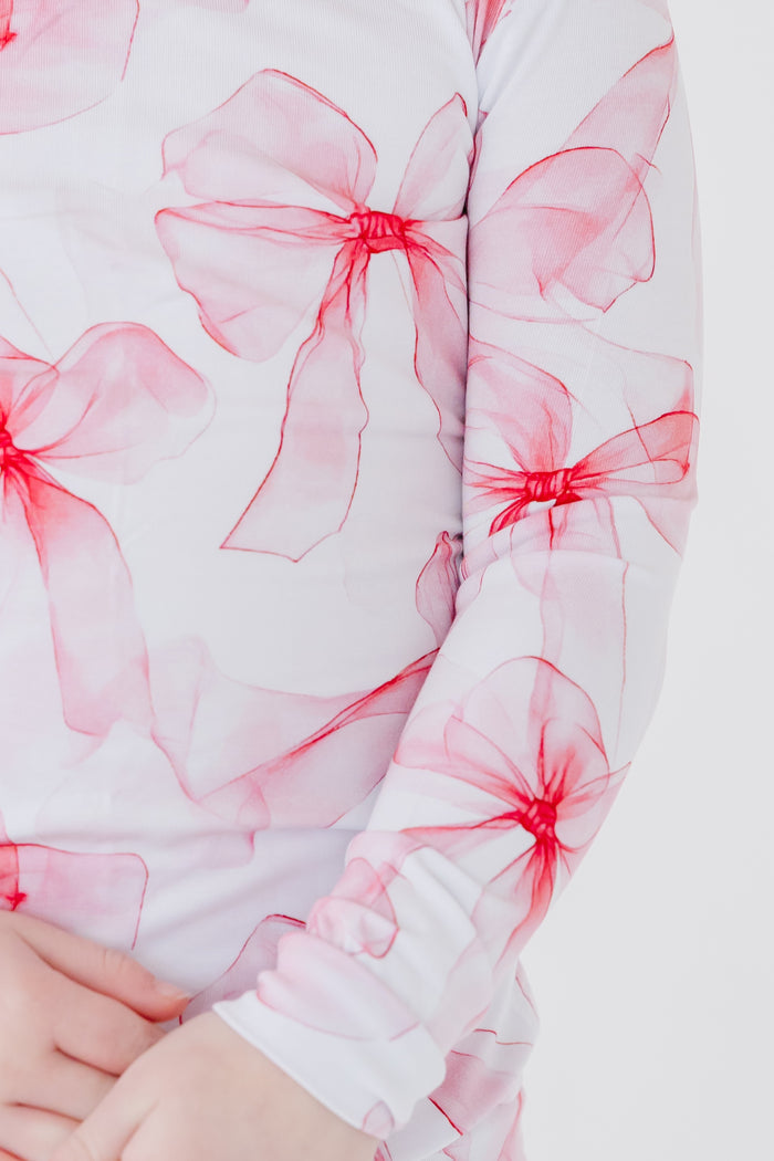 A close-up of a child in Jammie Session's Pretty in Bows Long Sleeve PJ's‚Äîwhite kids' bamboo pajamas with a playful pink and red bow print.