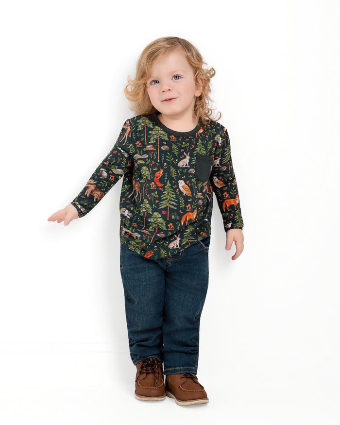 A young child with long blonde hair stands against a white background, wearing Jammie Session‚Äôs Wood You Be My Friend Kids' Long Sleeve T-shirt, blue jeans, and brown shoes.
