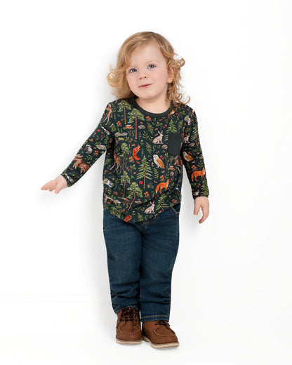 A young child with long blonde hair stands against a white background, wearing Jammie Session‚Äôs Wood You Be My Friend Kids' Long Sleeve T-shirt, blue jeans, and brown shoes.
