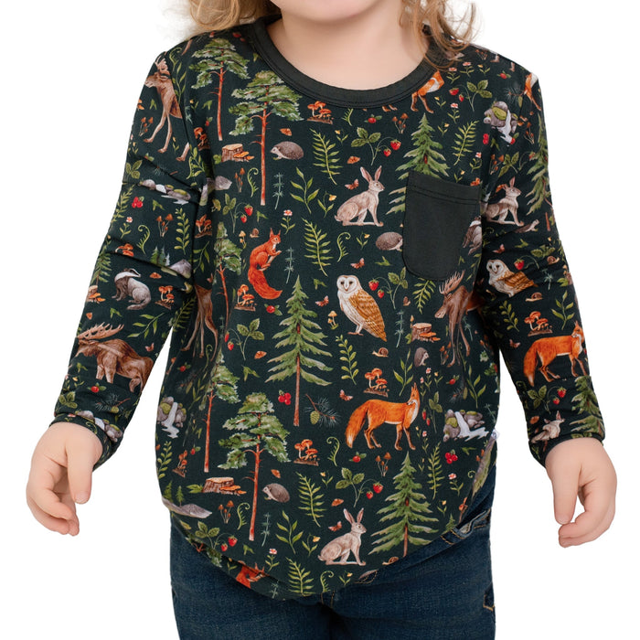 A child wears the Jammie Session "Wood You Be My Friend" Kids' Long Sleeve T-shirt, showcasing a dark forest print with trees and animals‚Äîperfect hypoallergenic clothing for adventurous kids, paired here with dark pants.