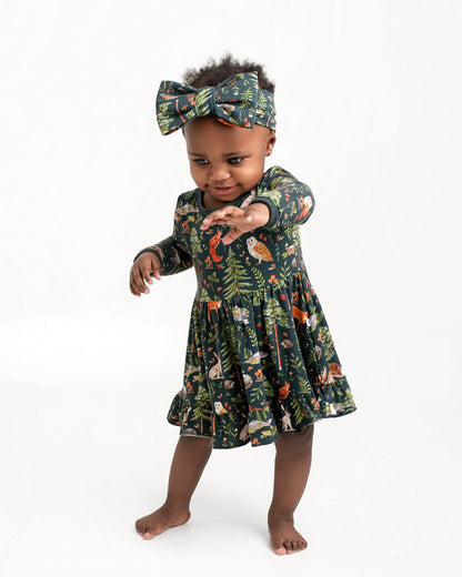 A toddler in a Jammie Session Wood You Be My Friend Long Sleeve Bodysuit Twirl Dress and matching headband stands barefoot against a plain white background, reaching one arm forward.